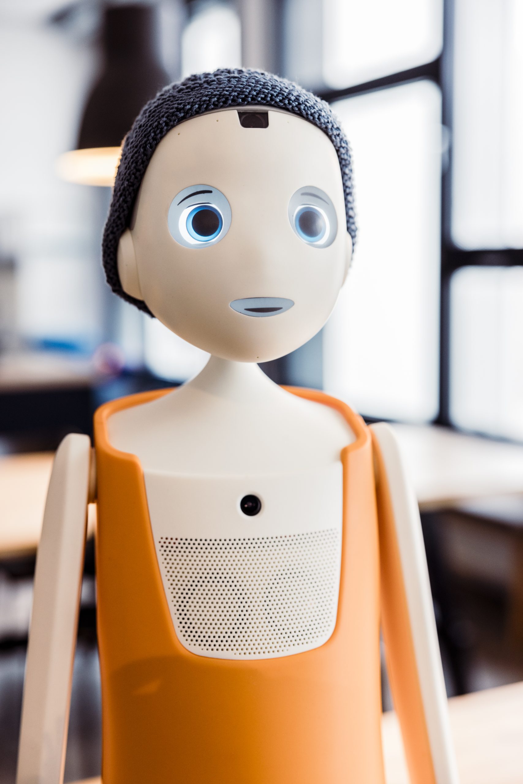 Der soziale Roboter Navel mit oranger Körperschale, gestrickter Mütze und großen runden Augen in einem hellen Raum